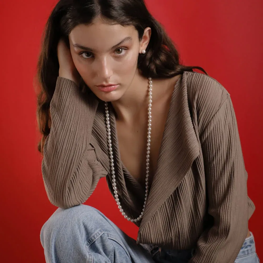 Lange Perlenkette an einem Model mit braunem Pullover vor lebhaftem rotem Hintergrund, mittlere Einstellung.