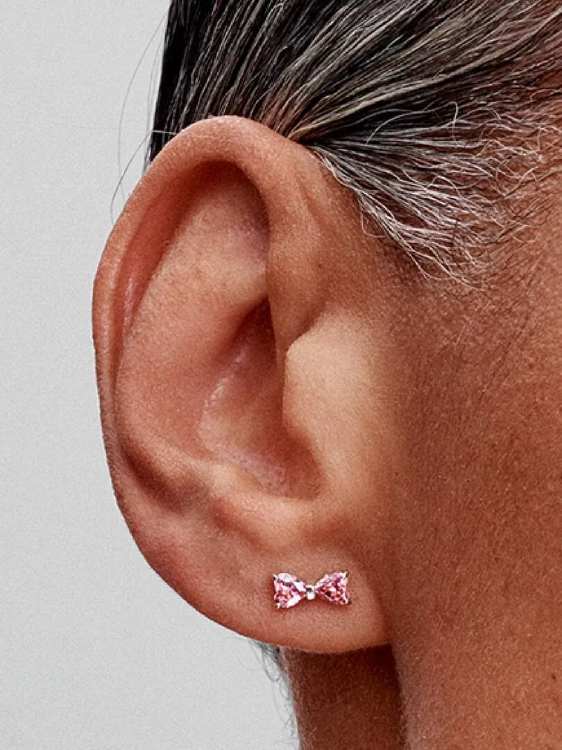 Close-up side view of a pink bow stud earring with cubic zirconia worn on an earlobe.