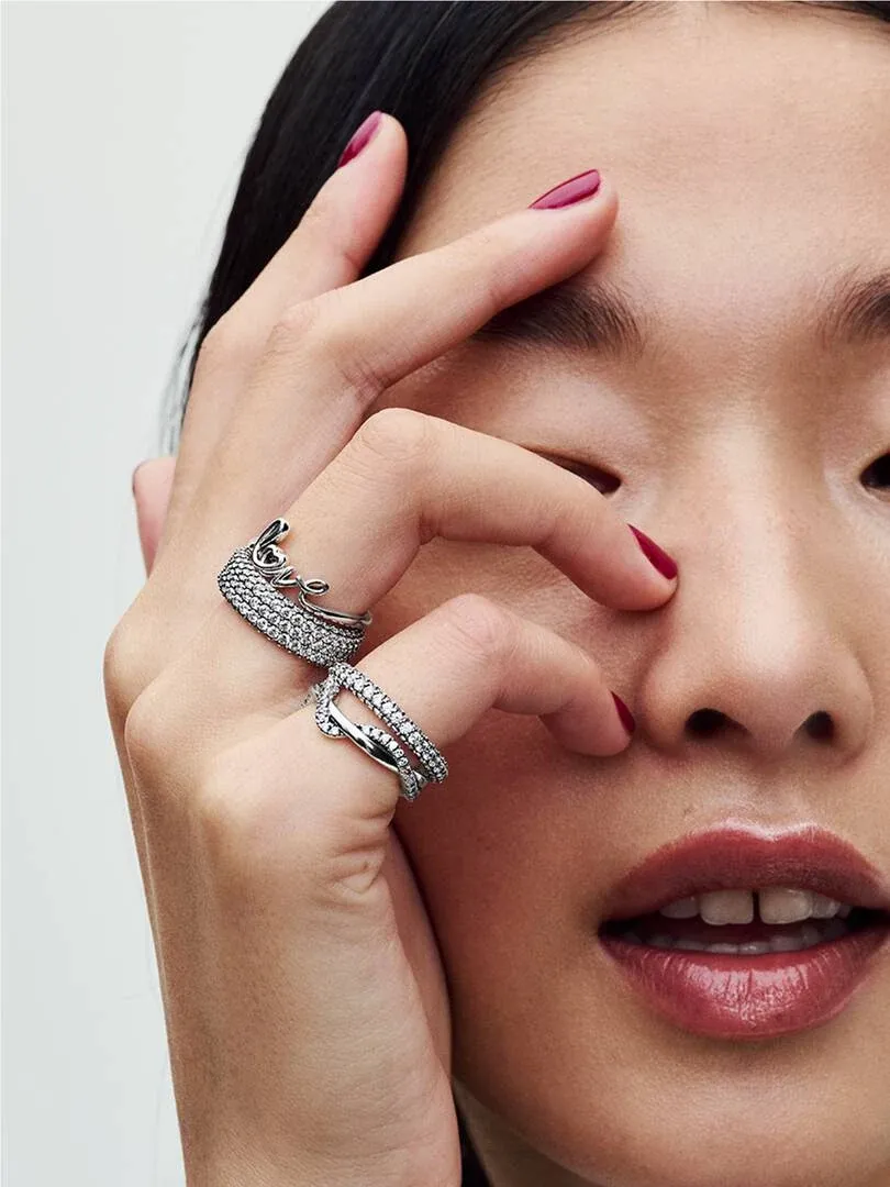 Primer plano de dos anillos entrelazados en un dedo, mano sobre el rostro, fondo neutro.