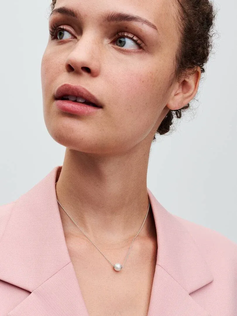 Primer plano del collar con perla sobre el cuello de una modelo, vistiendo una chaqueta rosa claro.