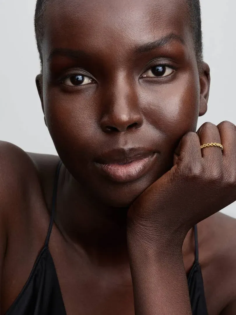 Nahaufnahme einer Hand am Kinn, die den goldenen Ring mit Herzfiligran zeigt.