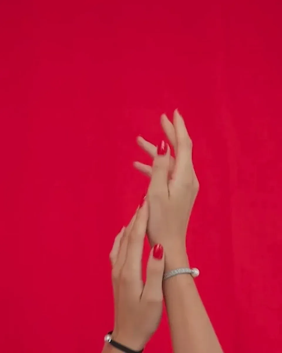 Nahaufnahme des Armbands an einem Handgelenk mit rotem Nagellack, leuchtend roter Hintergrund, vertikale Aufnahme.