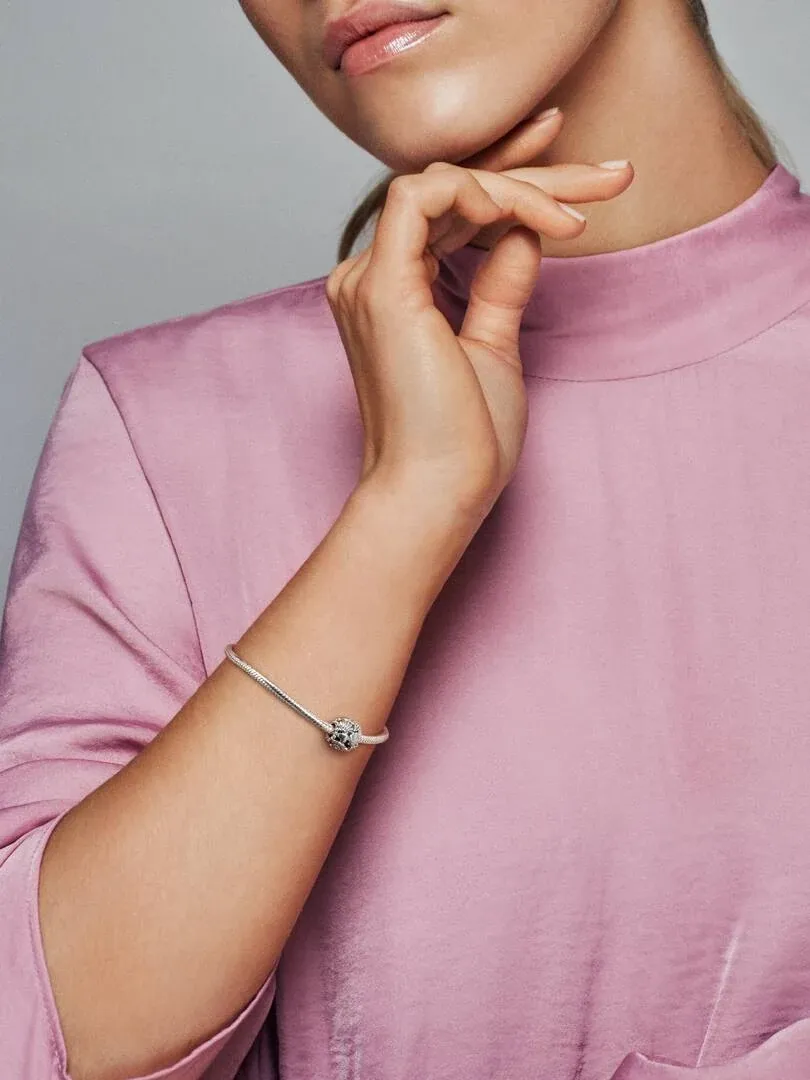 Close-up of the charm on a model's wrist, side view with soft pink blouse.