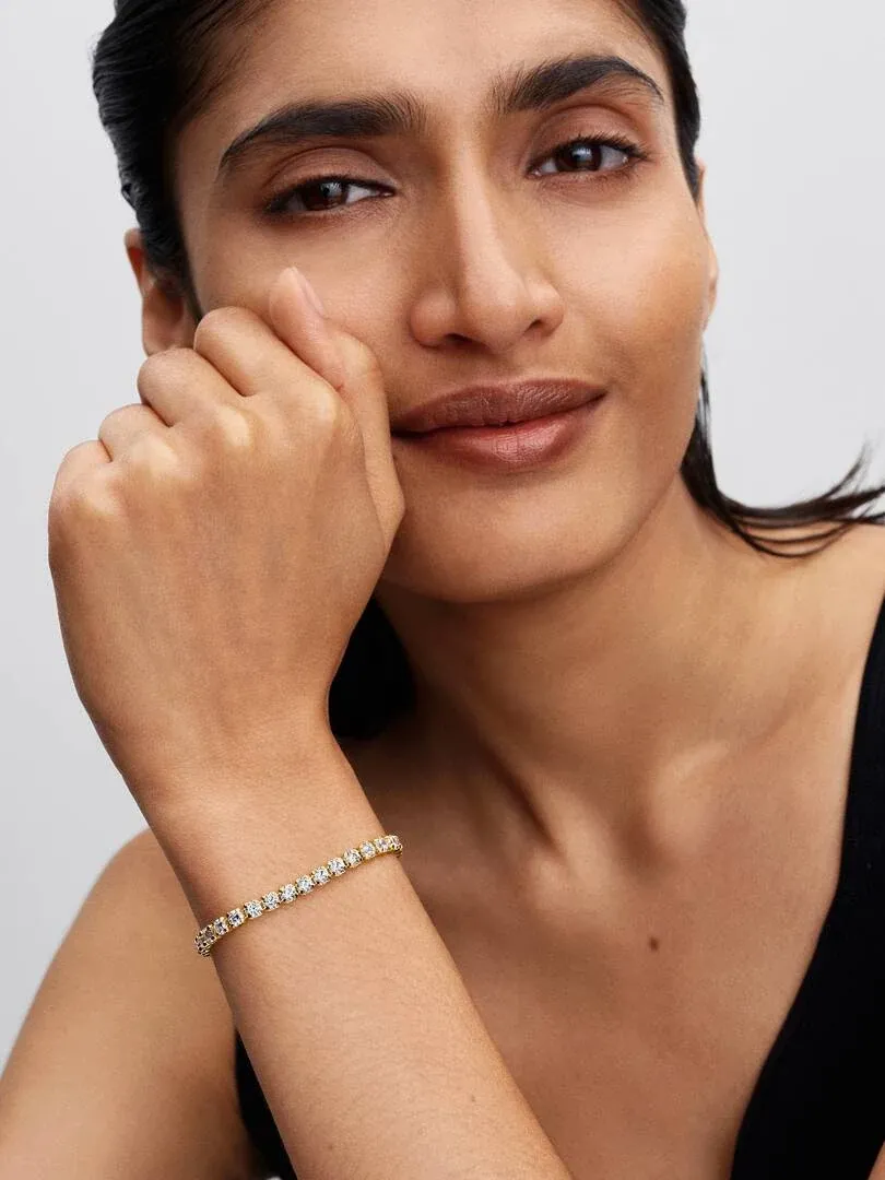 Close-up van een gouden tennisarmband met zirkonia om de pols van een model, lichte neutrale achtergrond.