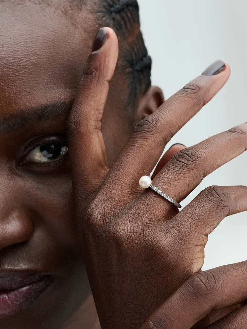 Close-up of the pearl ring on the middle finger, side view against a neutral background.