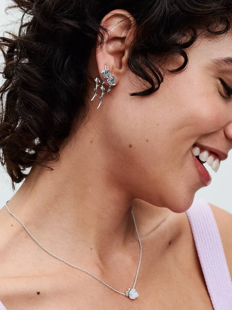 Zijaanzicht van een lachend model met een rozenoorbel en zilveren ketting op de huid.