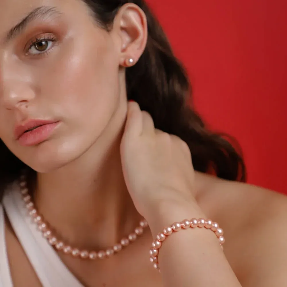 Primer plano de modelo luciendo collar y pulsera de perlas rosas sobre fondo rojo vibrante.