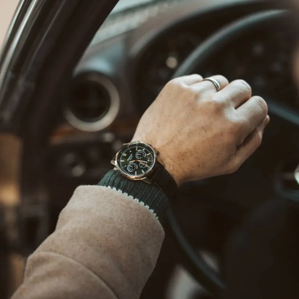 Reloj puesto en muñeca masculina sujetando el volante de un coche, fondo desenfocado del interior del vehículo.