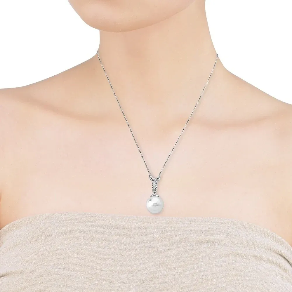 Collar con perla blanca sobre cuello de modelo, toma frontal de plano medio en fondo neutro.
