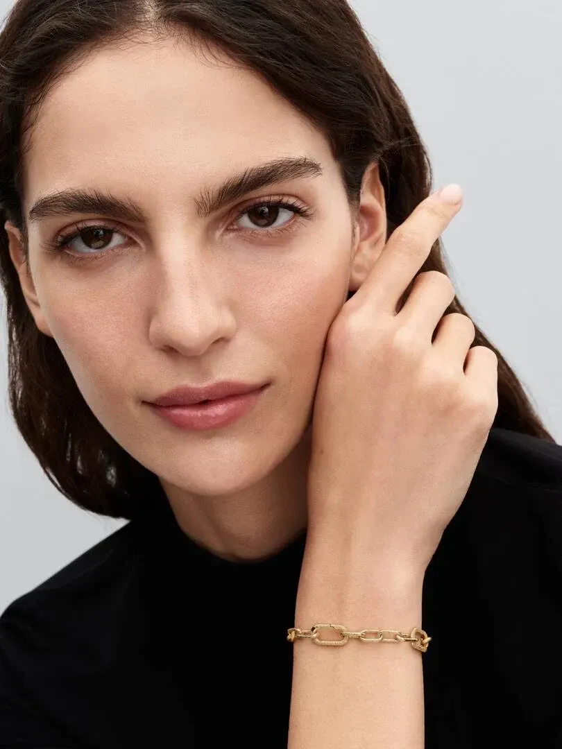 Close-up of the gold link bracelet on a wrist, side view with model against a neutral gray background.