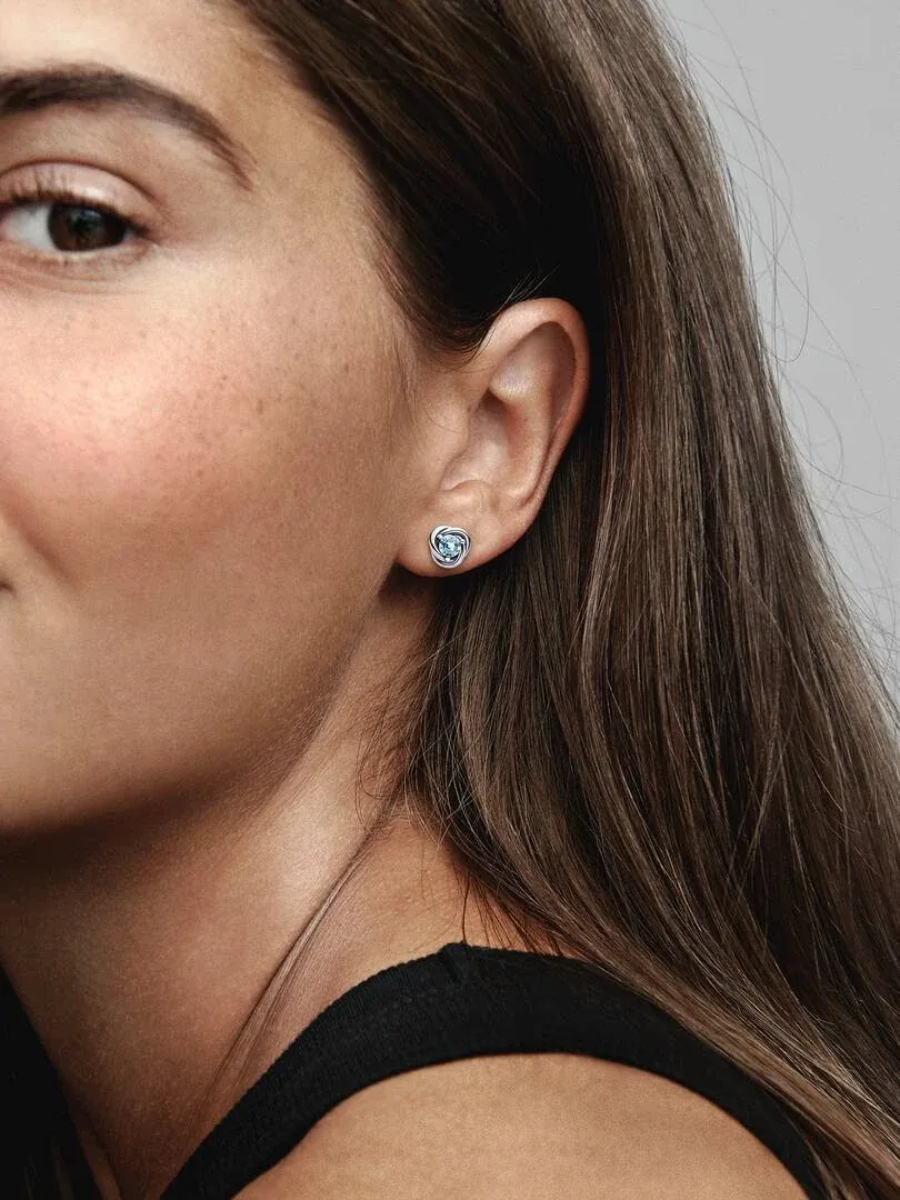 Seitenansicht Nahaufnahme eines Ohrsteckers mit hellblauem Kristall am Ohrläppchen, unscharfer Hintergrund.