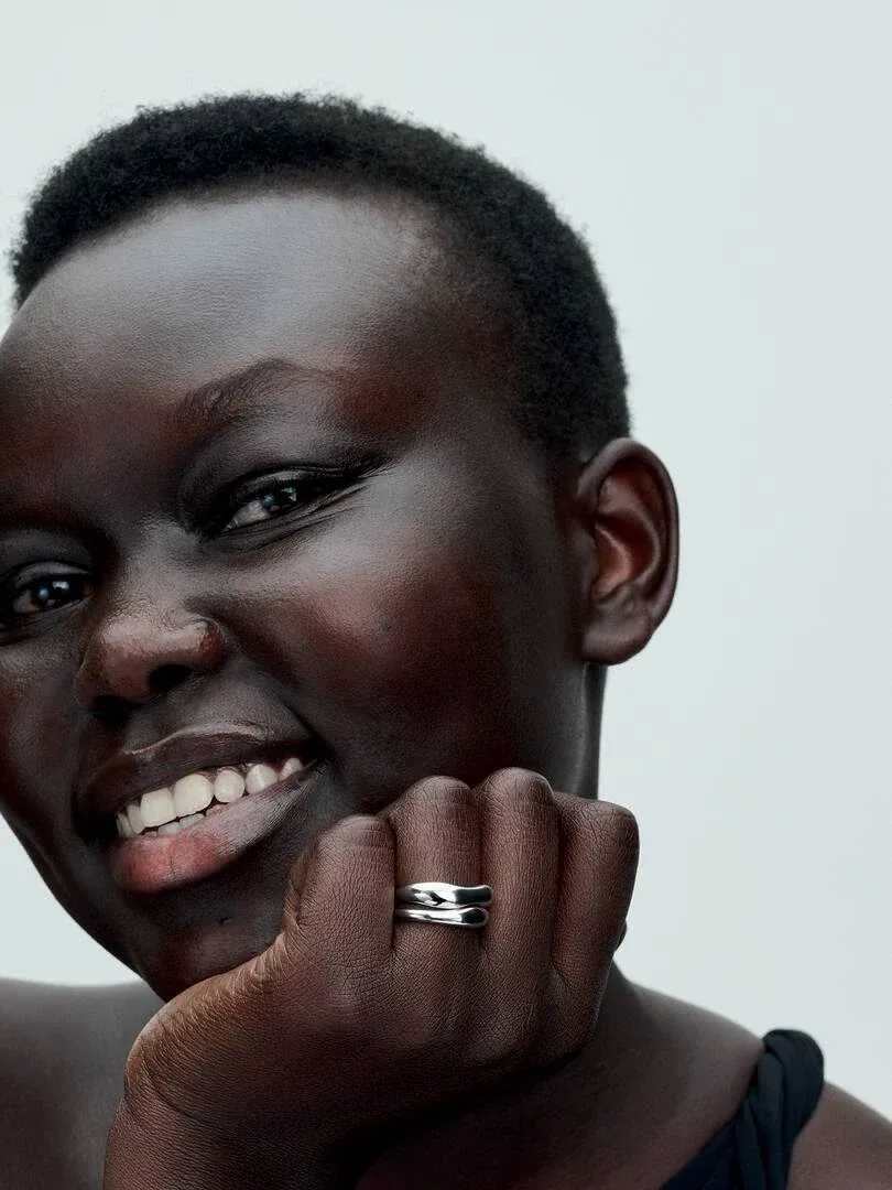 Gros plan de bagues organiques en argent portées au doigt, main posée sous le menton.