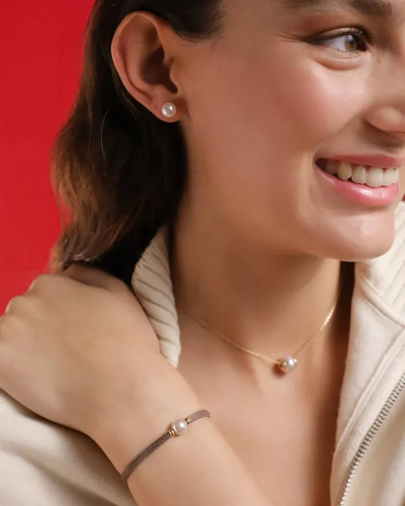 Mujer sonriente con pendientes de perla, collar y pulsera taupe, fondo rojo vibrante.