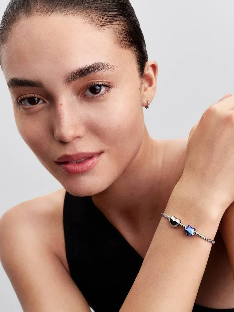 Close-up van een pols met een zilveren armband en blauwe ster charm, model tegen een neutrale achtergrond.