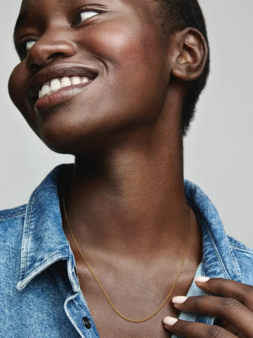 Gros plan d'un collier doré sur le cou d'un modèle, vue de profil avec une chemise en jean.