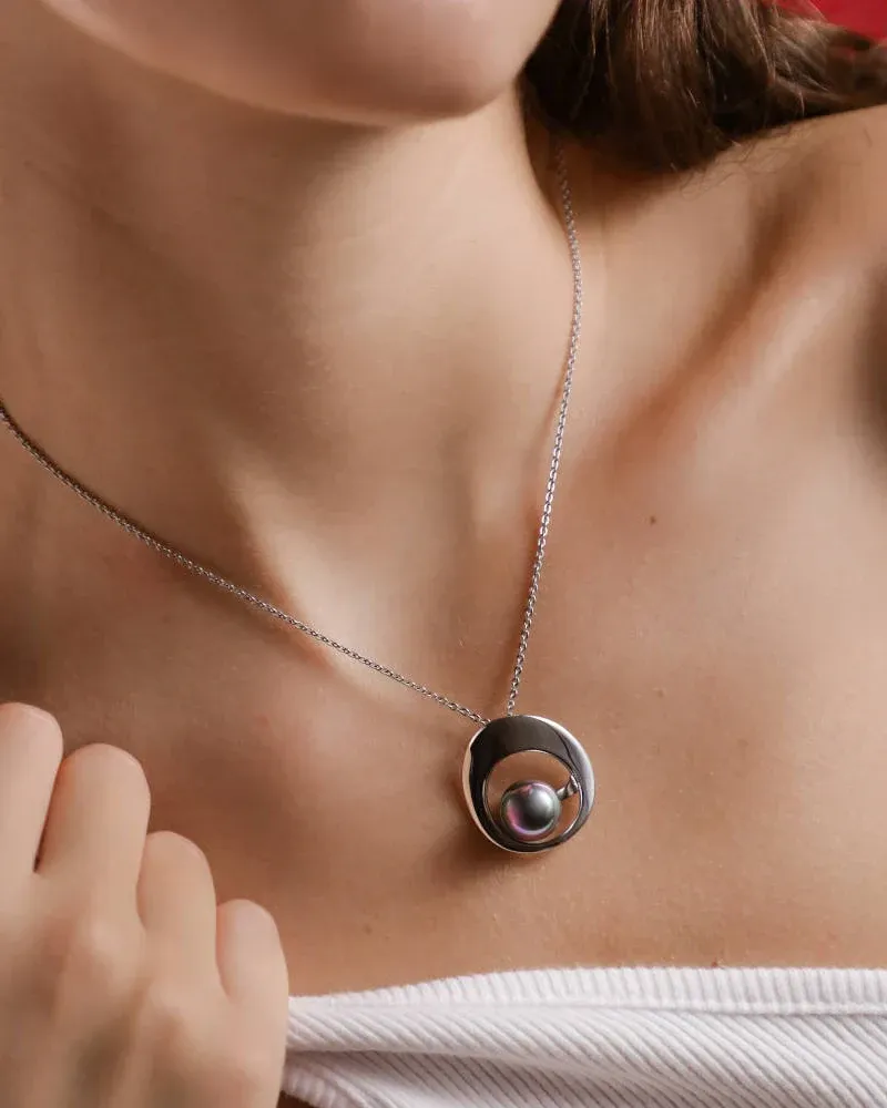 Close-up of the grey pearl pendant on a model's neck, front view with soft blurred background.
