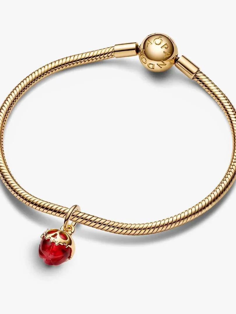 Roter Apfel-Charm an einem goldenen Armband, Draufsicht aus einem Winkel, neutraler weißer Hintergrund.