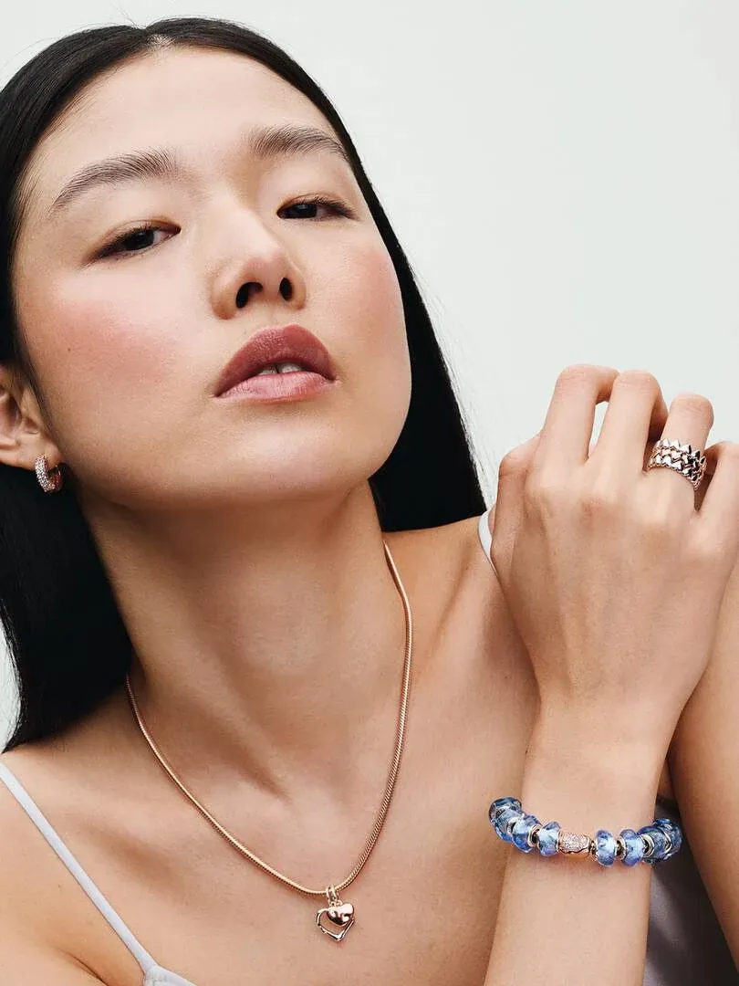 Close-up of model wearing a chain necklace, earrings, and beaded bracelet against a white background.
