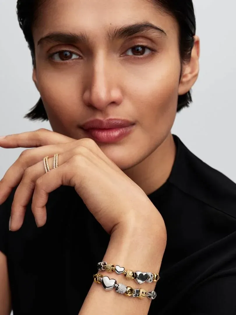 Close-up of hand and wrist wearing thin rings and charm bracelet against a neutral background.