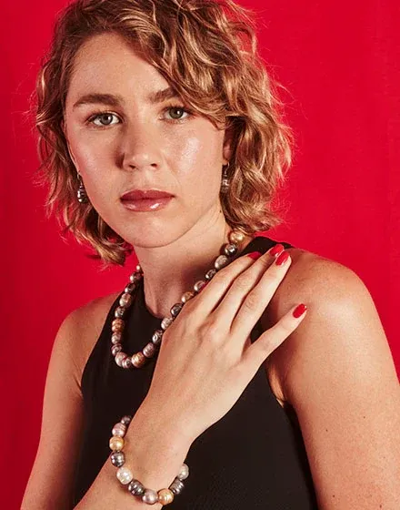 Modelo con collar y pulsera de perlas barrocas sobre fondo rojo vibrante, plano medio corto.
