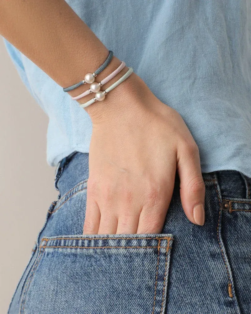 Tres pulseras de cordón con perlas puestas en la muñeca, modelo con camisa azul y vaqueros, plano medio.