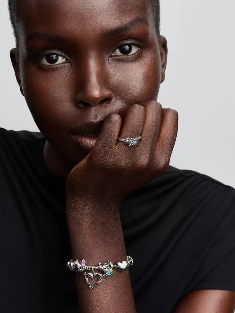 Nahaufnahme einer Hand mit Armband und Ring, Modell vor neutralem grauem Hintergrund, Frontalansicht.