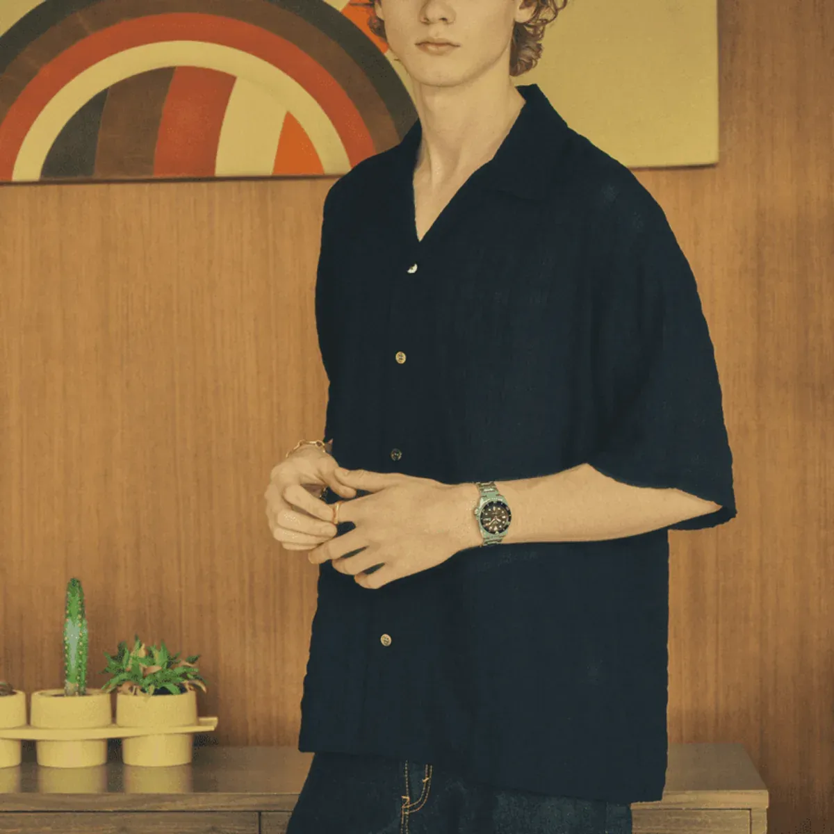 Man wearing a dark shirt and watch on the wrist, wooden wall background with abstract painting.
