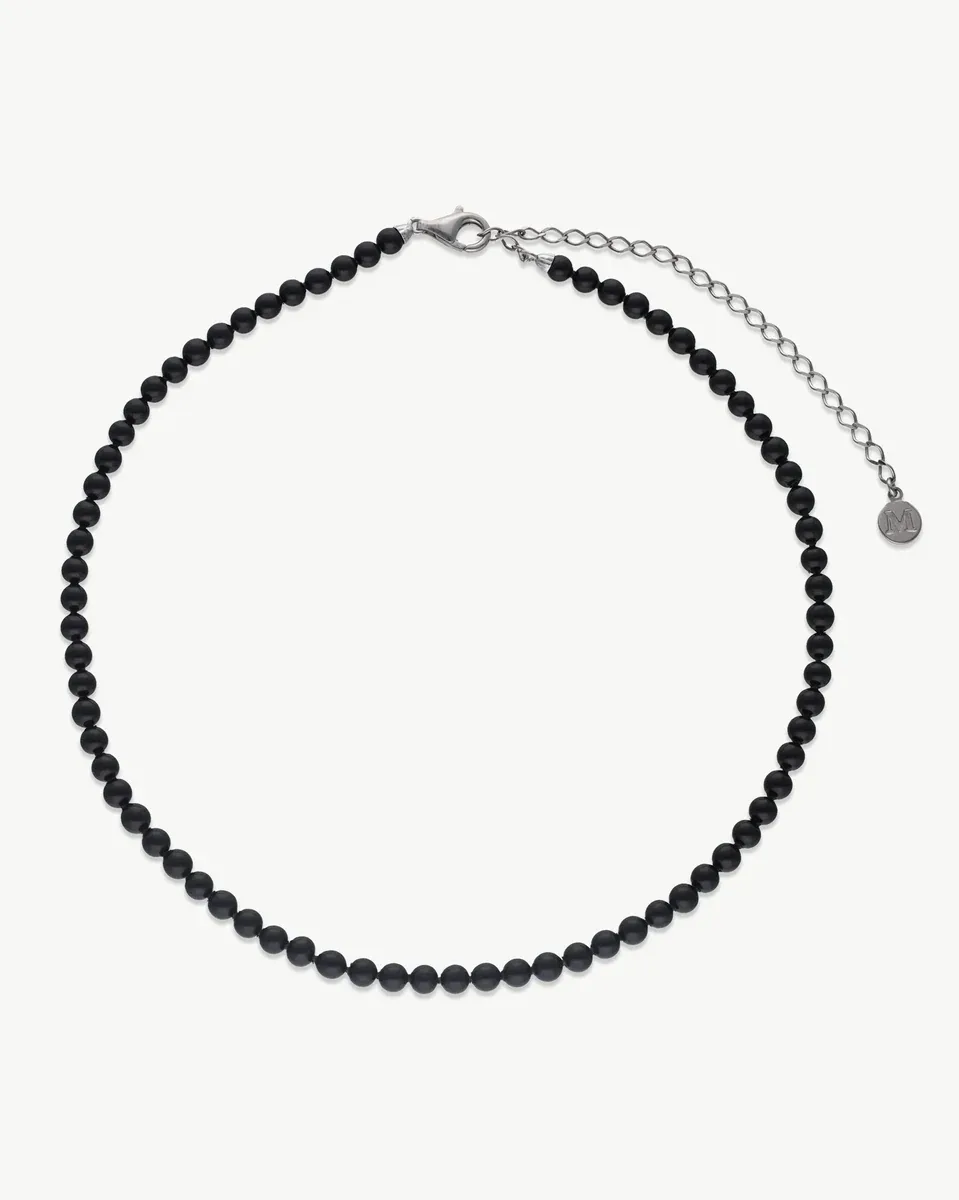Collar de perlas negras dispuesto en círculo sobre fondo blanco, vista frontal con cierre y cadena de plata.