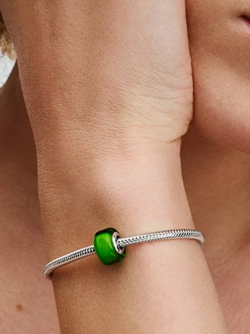 Close-up of a green glass charm on a silver bracelet, worn on a model's wrist.