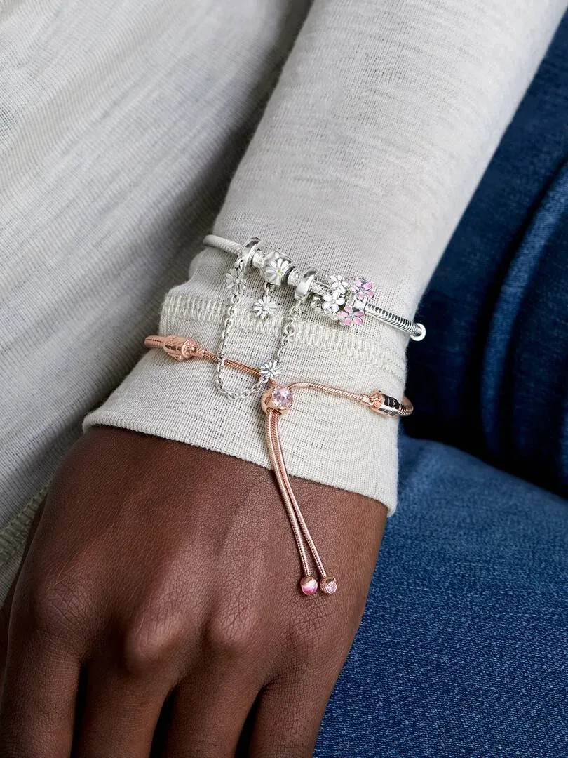 Close-up van een armband met charms om de pols, zijaanzicht over witte mouw en wazige blauwe achtergrond.