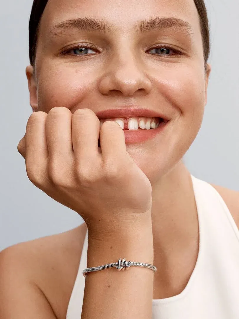 Nahaufnahme des Pfeil-Charms an einem Armband am Handgelenk, lächelndes Modell vor neutralem Hintergrund.