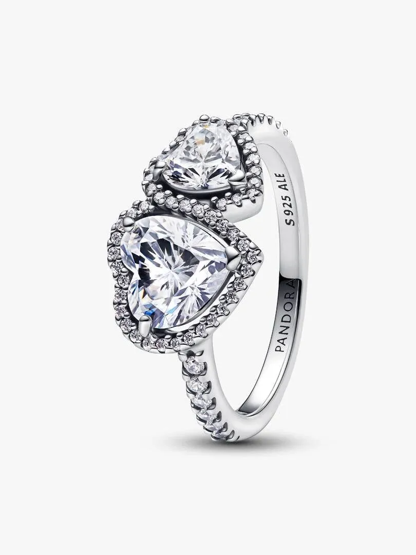 Anillo de plata con dos gemas en forma de corazón, vista lateral en ángulo sobre fondo blanco.