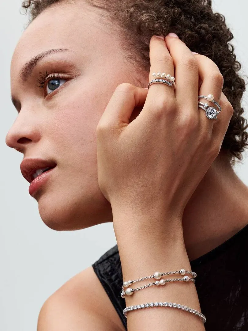 Nahaufnahme von Handgelenk und Hand mit Perlen- und Zirkonia-Armbändern vor neutralem Hintergrund.