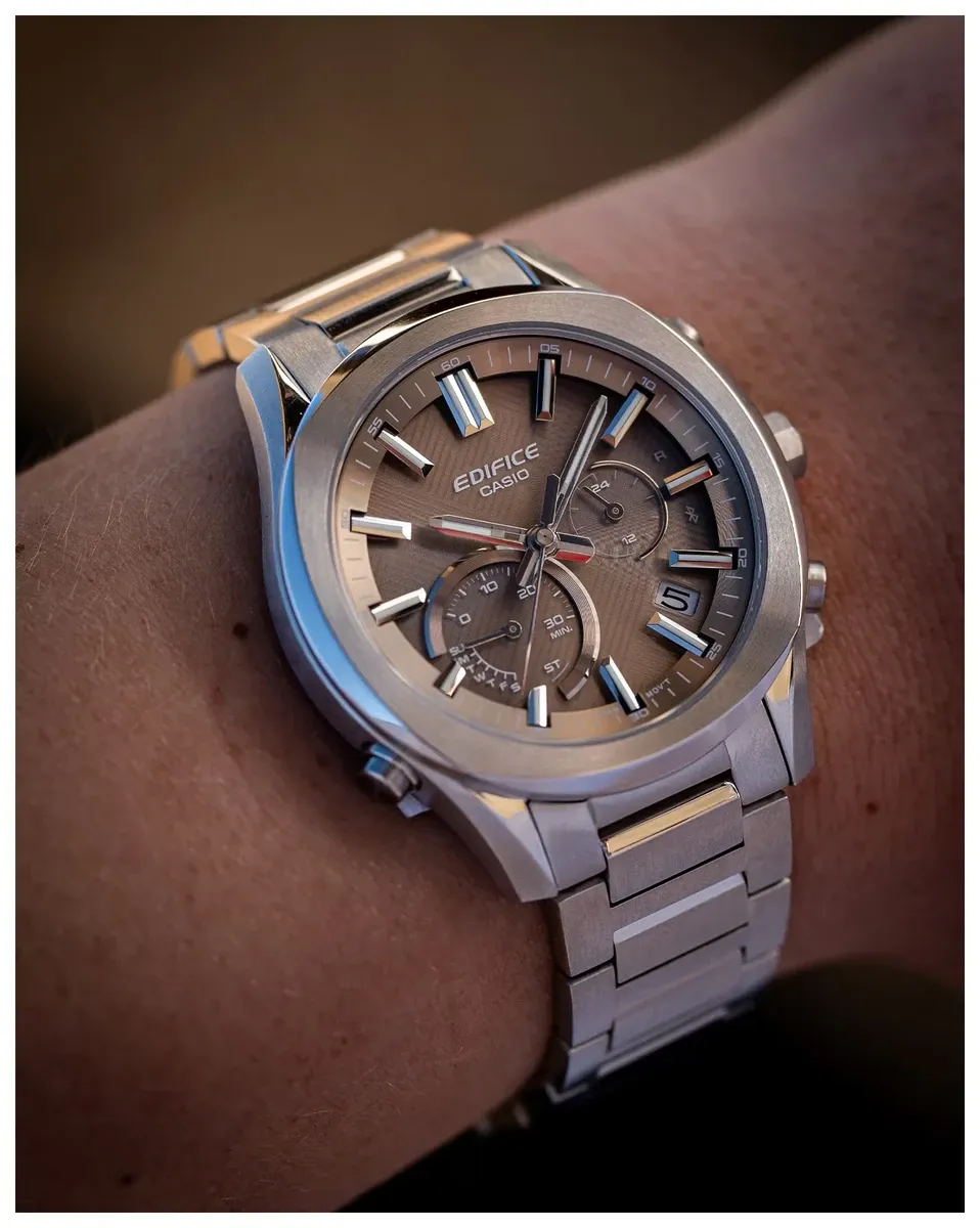 Reloj puesto en la muñeca, toma en ángulo primer plano, fondo desenfocado en tonos cálidos.