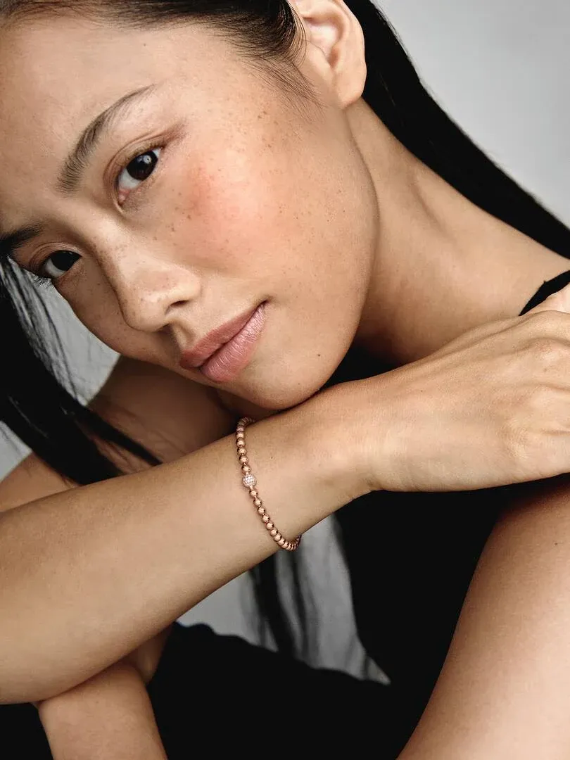 Nahaufnahme des Roségold-Perlenarmbands am Handgelenk eines Models, Seitenansicht vor neutralem Hintergrund.