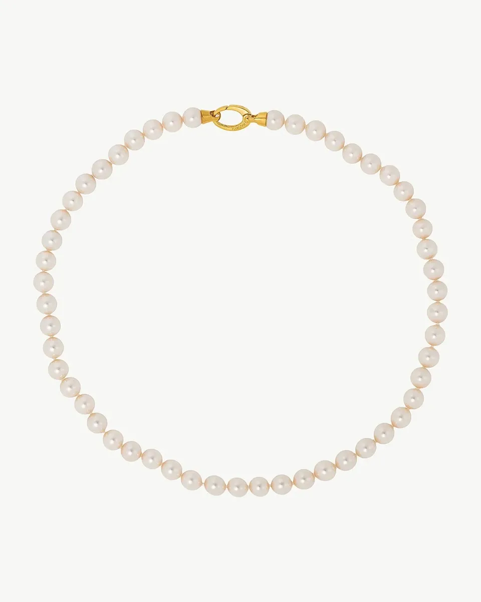 Collar de perlas dispuesto en círculo sobre fondo blanco, vista cenital con detalle del cierre dorado.