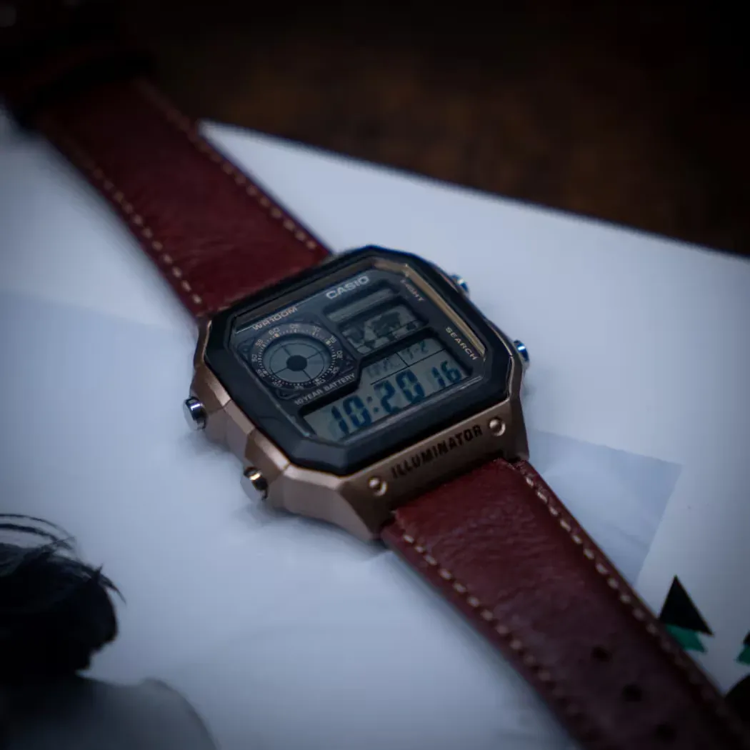 Reloj visto desde un ángulo cenital diagonal, apoyado sobre una superficie blanca con fondo desenfocado.