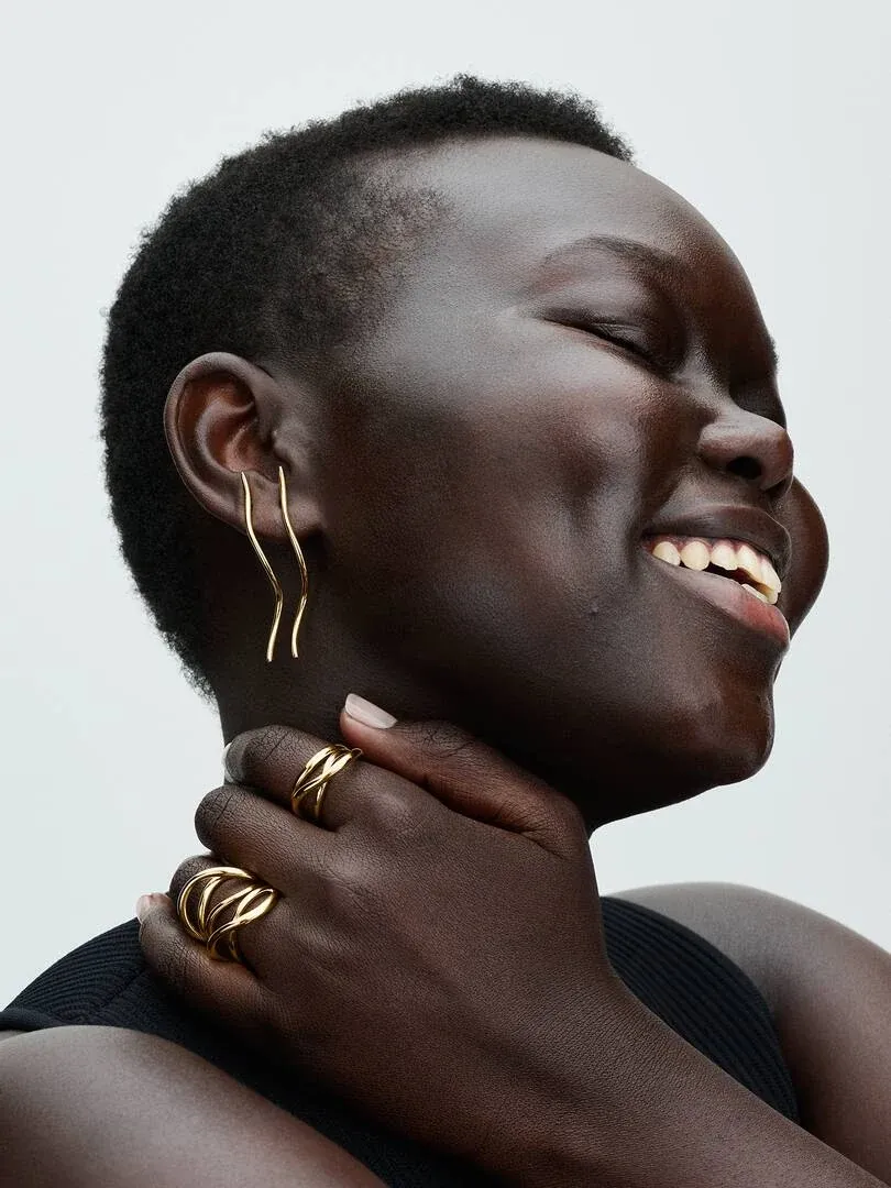 Gros plan de profil d'un modèle portant des bagues et boucles d'oreilles dorées sur fond blanc.