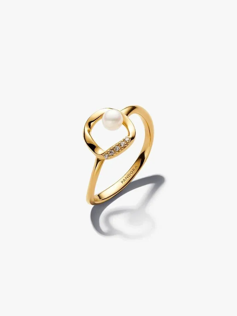 Gold ring with white pearl and pavé stones, side angle view on a white background with soft shadow.