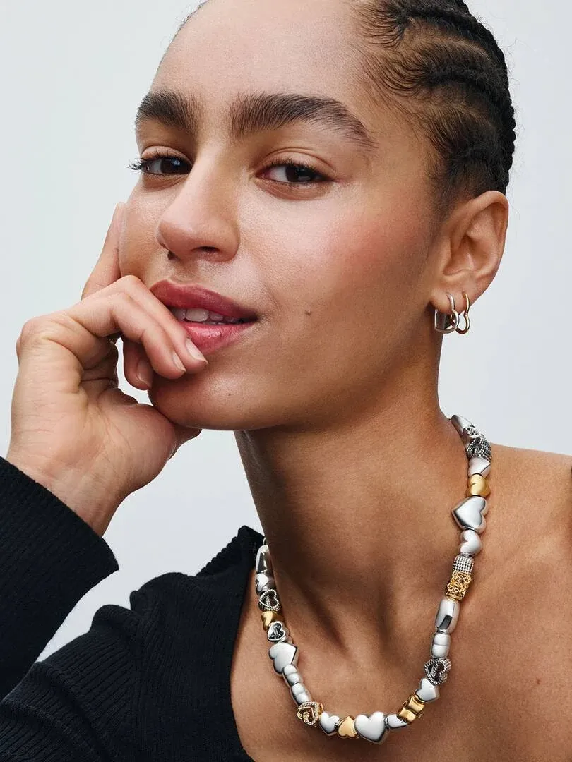 Gros plan d'un modèle portant un collier aux cœurs entrelacés, vue de profil sur fond blanc.