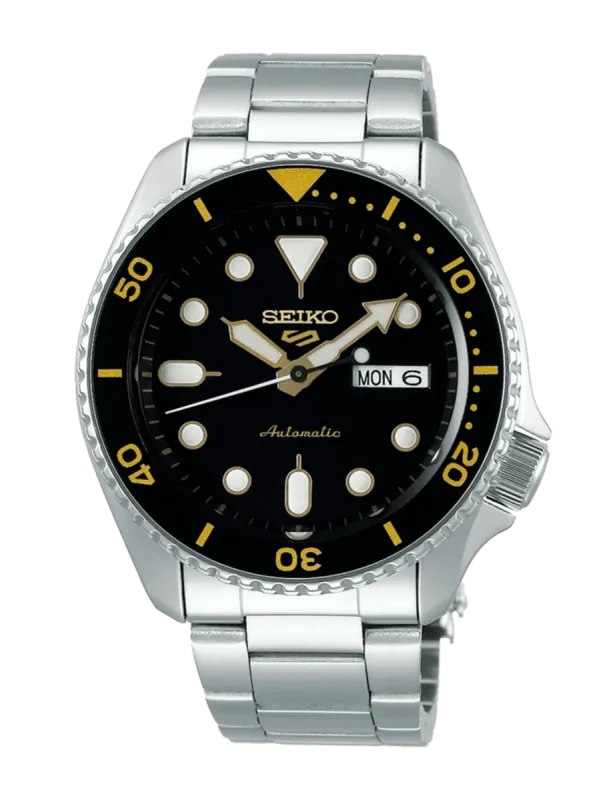 Vista frontal del reloj con esfera negra y detalles dorados, brazalete de acero inoxidable, fondo blanco.