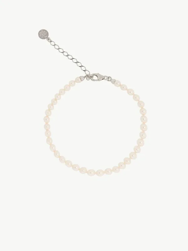 Pulsera de perlas dispuesta en círculo sobre fondo blanco, vista cenital con detalle del cierre y cadena extensora.