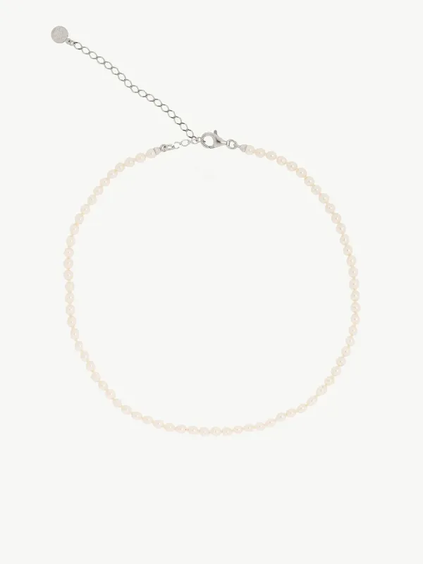 Collar de perlas dispuesto en círculo sobre fondo blanco, vista cenital con detalle del cierre y cadena extensora.