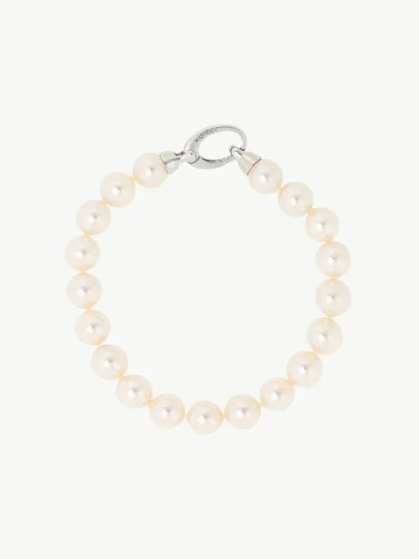 Pulsera de perlas blancas dispuesta en círculo sobre fondo blanco, vista cenital con detalle del cierre de plata.