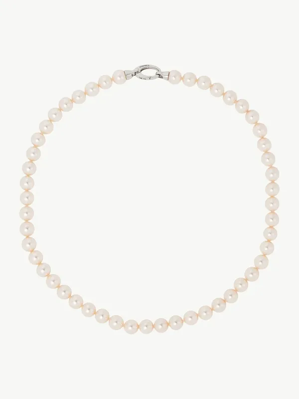 Collar de perlas dispuesto en círculo sobre fondo blanco, vista cenital con detalle del cierre superior.
