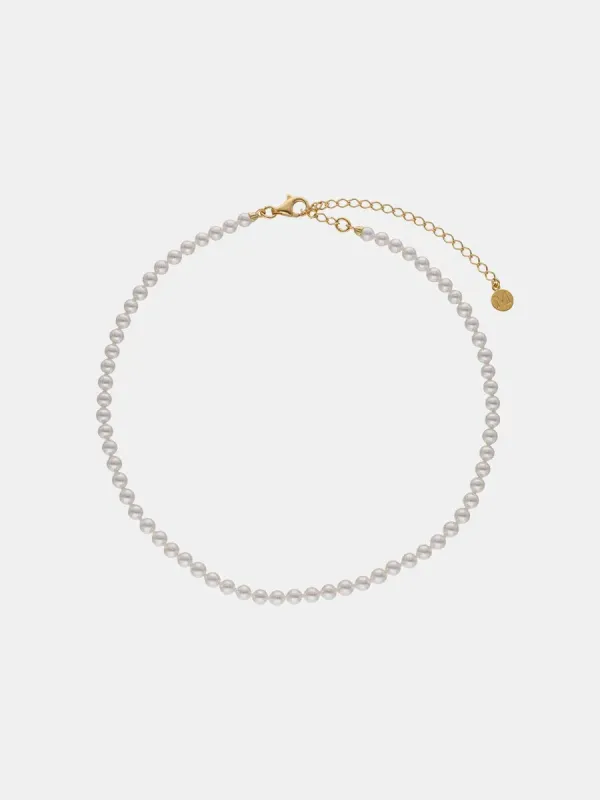 Collar de perlas dispuesto en círculo sobre fondo neutro, vista cenital con detalle del cierre y cadena extensora.