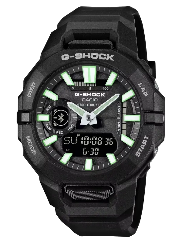 Vista frontal completa del reloj de resina negra con índices verdes, centrado sobre fondo negro.