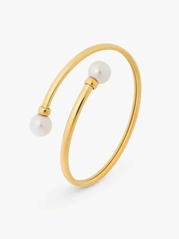 Brazalete rígido dorado con dos perlas blancas, vista en perspectiva sobre fondo blanco.