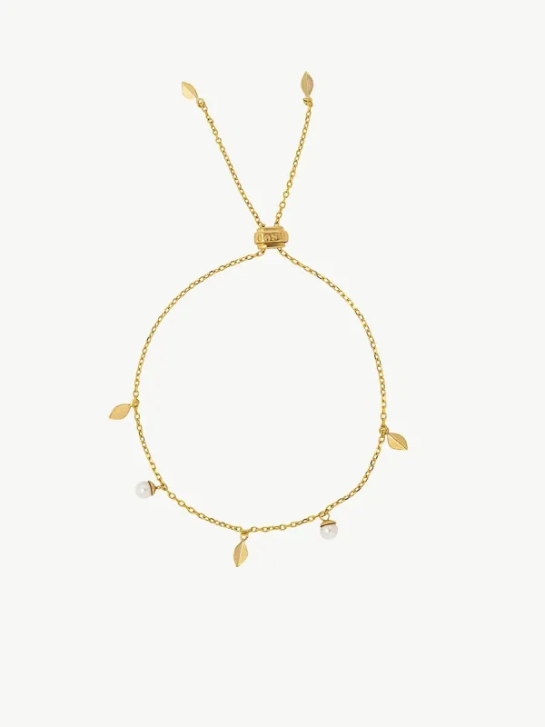 Vista cenital de pulsera ajustable dorada con perlas y hojas, dispuesta en círculo sobre fondo blanco.