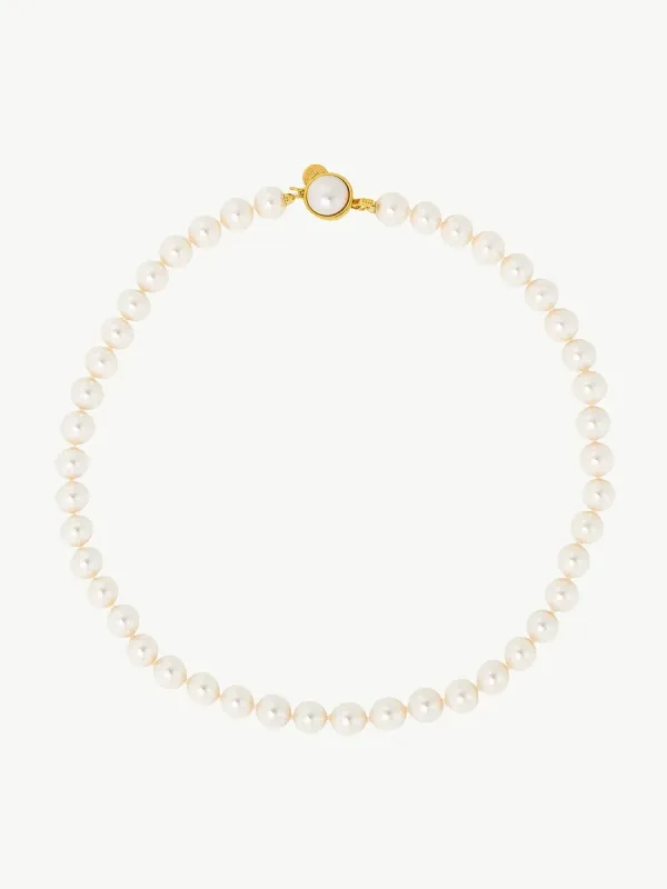 Collar de perlas dispuesto en círculo sobre fondo blanco, vista cenital con detalle del cierre dorado.